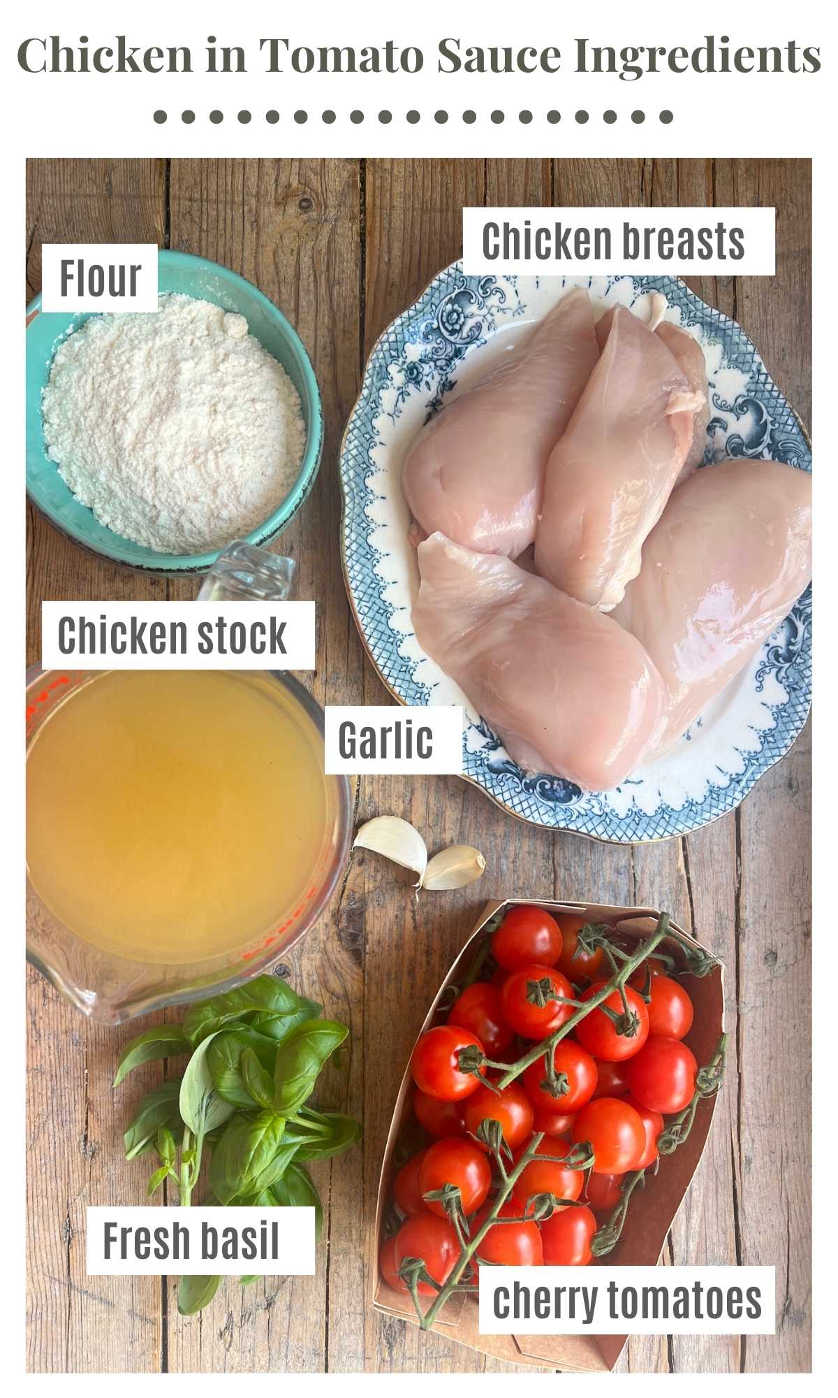 An overhead shot showing ingredients laid out on a rustic wooden board. The ingredients are labelled; flour, chicken breasts, cherry tomatoes, chicken stock, fresh basil, garlic.