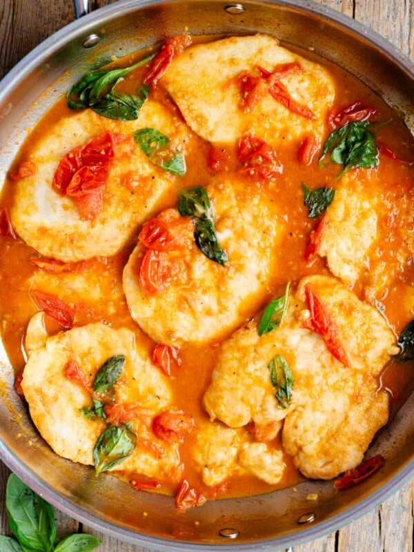 An overhead shot of chicken cutlets in a cherry tomato and basil sauce in a large pan.