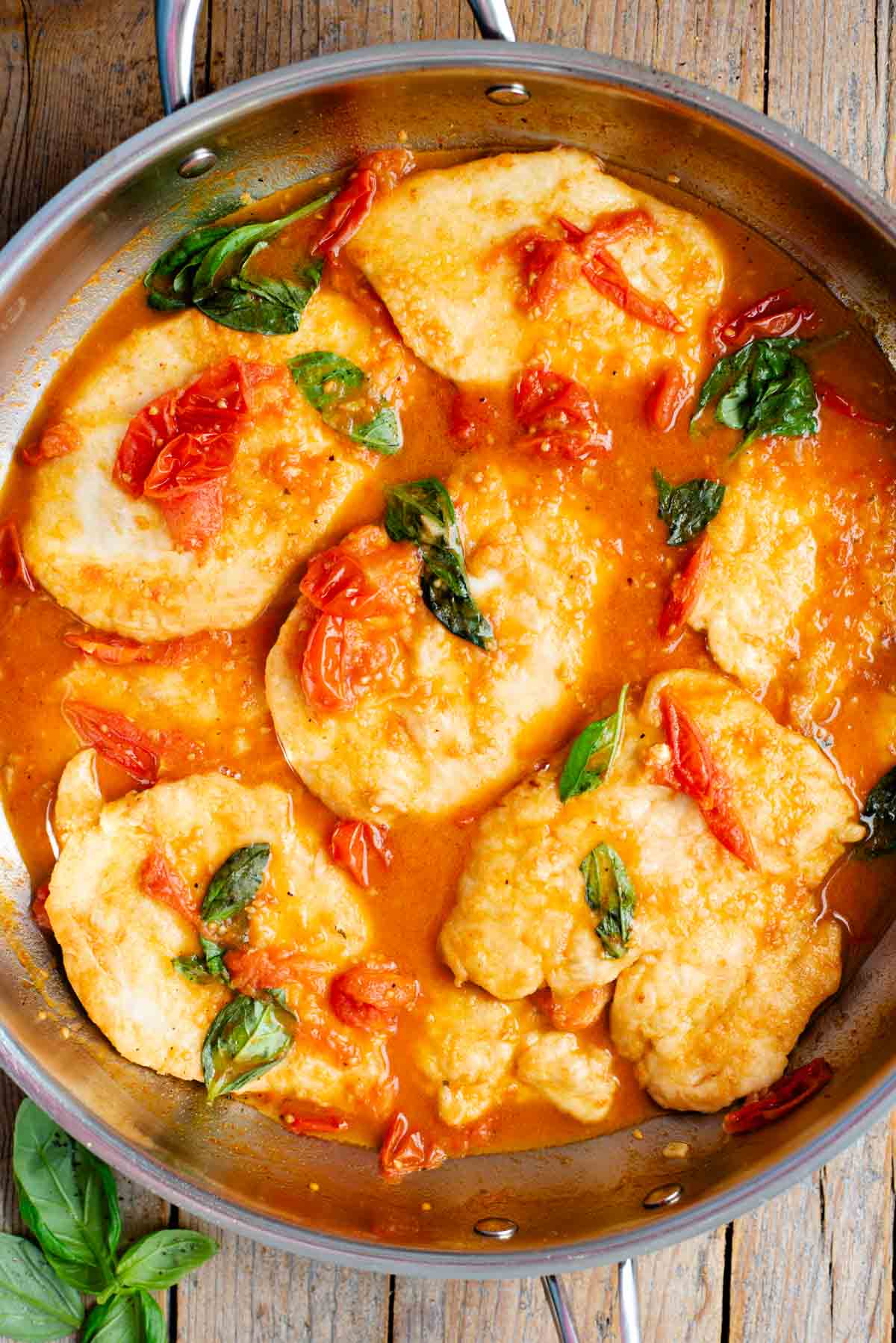 An overhead shot of chicken cutlets in a cherry tomato and basil sauce in a large pan.