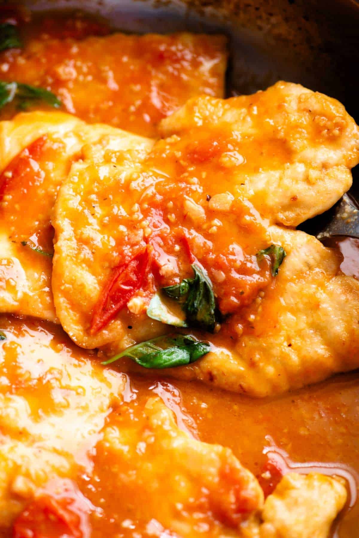 A close up of a piece on chicken in a pan covered in tomato and basil sauce.