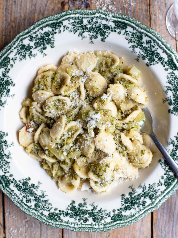 An overhead shot of orecchiette pasta with broccoli sauce in a green and white bowl on a rustic wooden background.