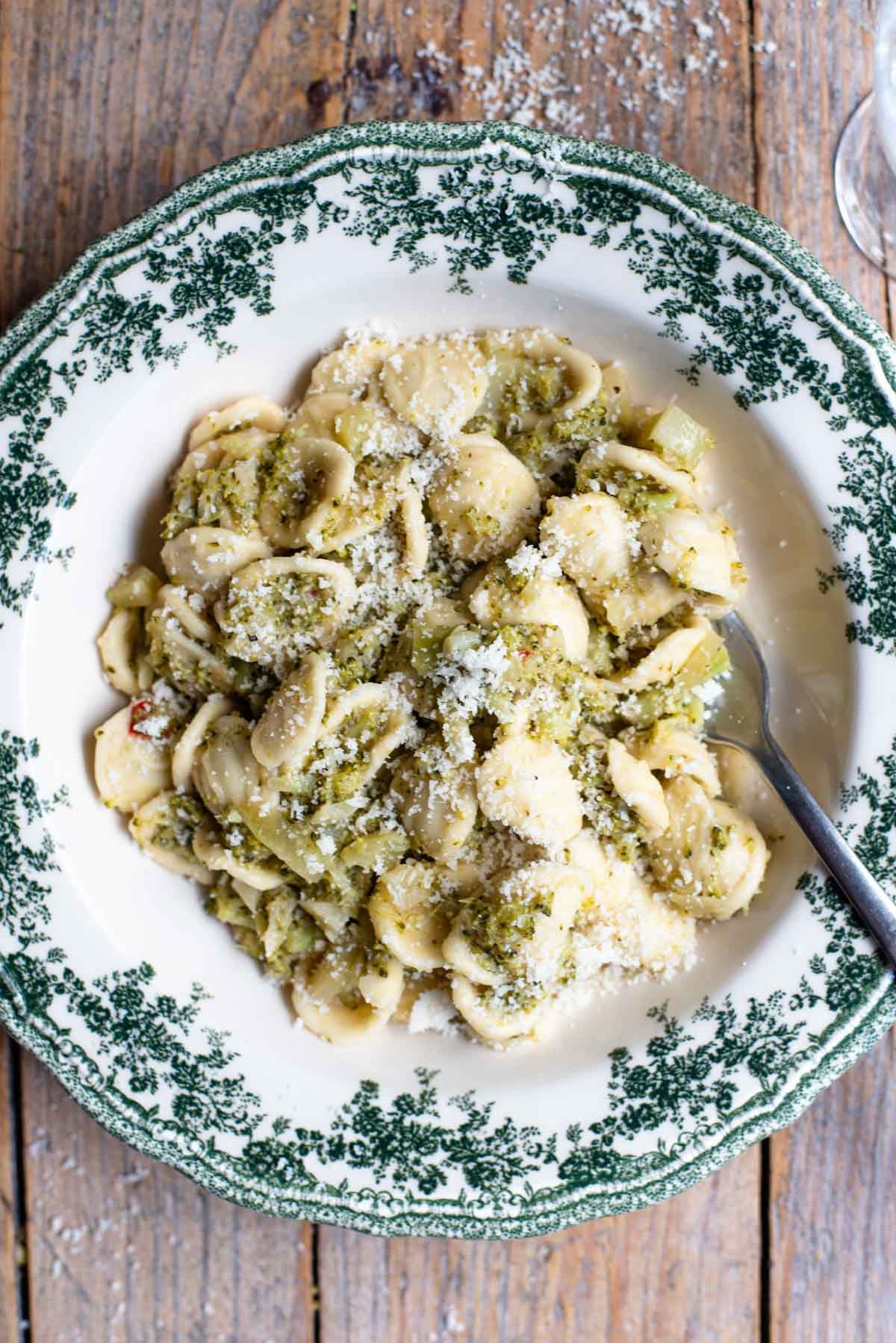 An overhead shot of orecchiette pasta with broccoli sauce in a green and white bowl on a rustic wooden background.