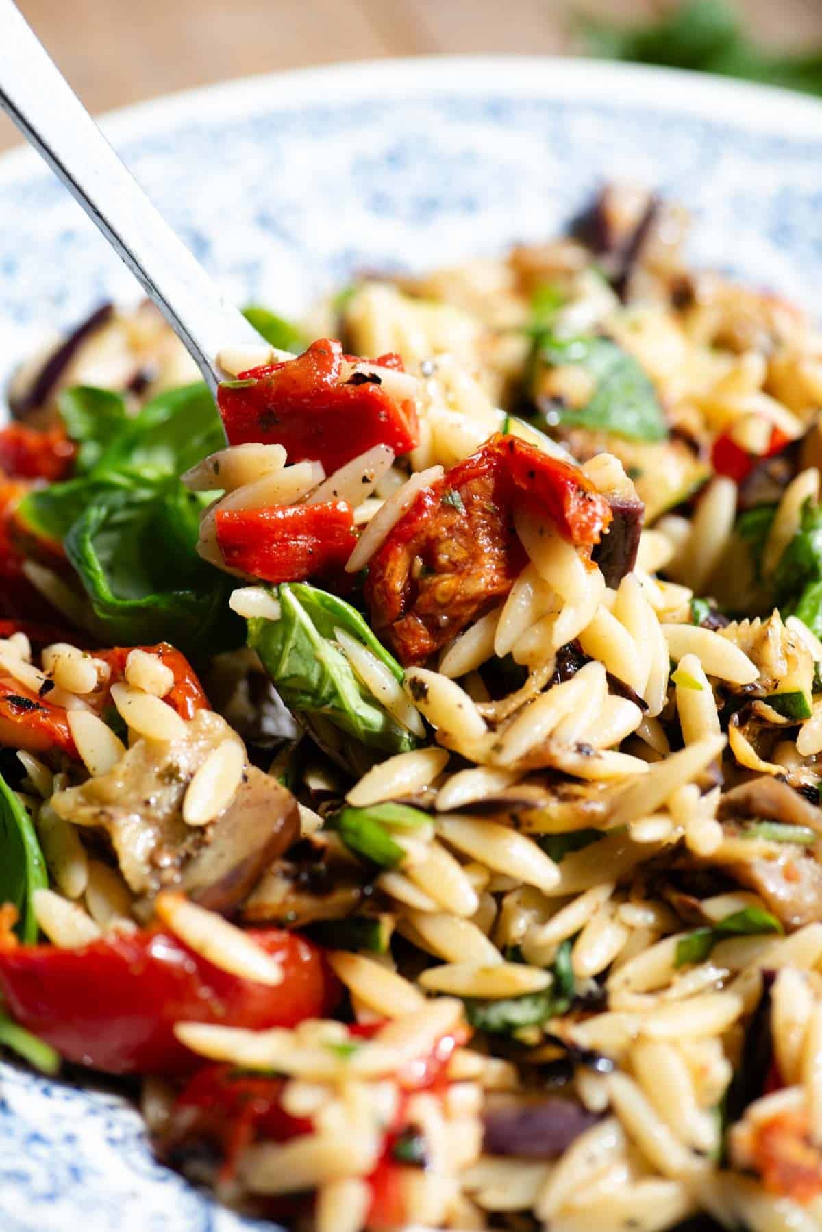A close up of an orzo pasta salad with tomatoes and grilled veg.