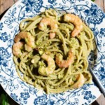 An overhead shot of shrimp and pistachio pesto pasta in a blue bowl on a rustic wooden surface.