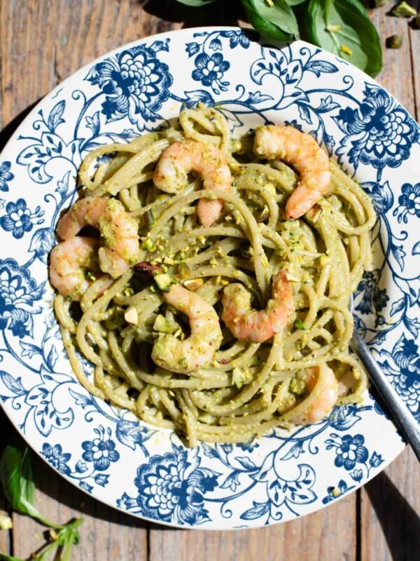 An overhead shot of pistachio pasta with shrimp in a blue floral bowl on a wooden background.