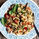An orzo pasta salad with grilled veg in a blue bowl on a rustic wooden surface.