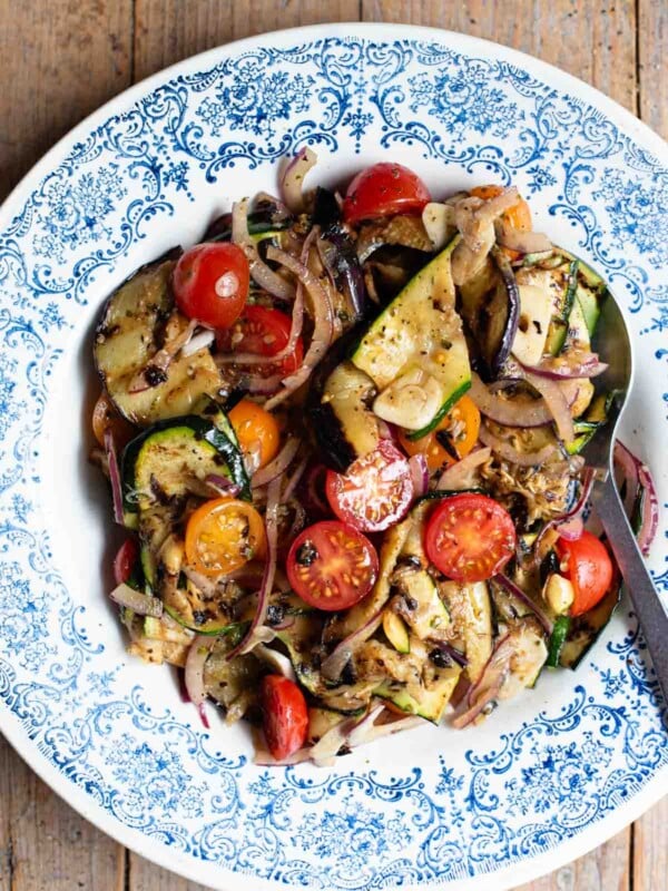 An overhead shot of marinated grilled summer vegetables in a blue bowl on a wooden surface.