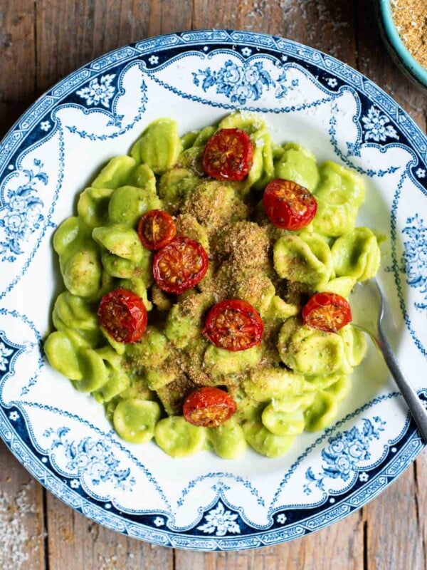 An overhead shot of orecchiette pasta in a vibrant green zucchini sauce with roasted cherry tomatoes on top.
