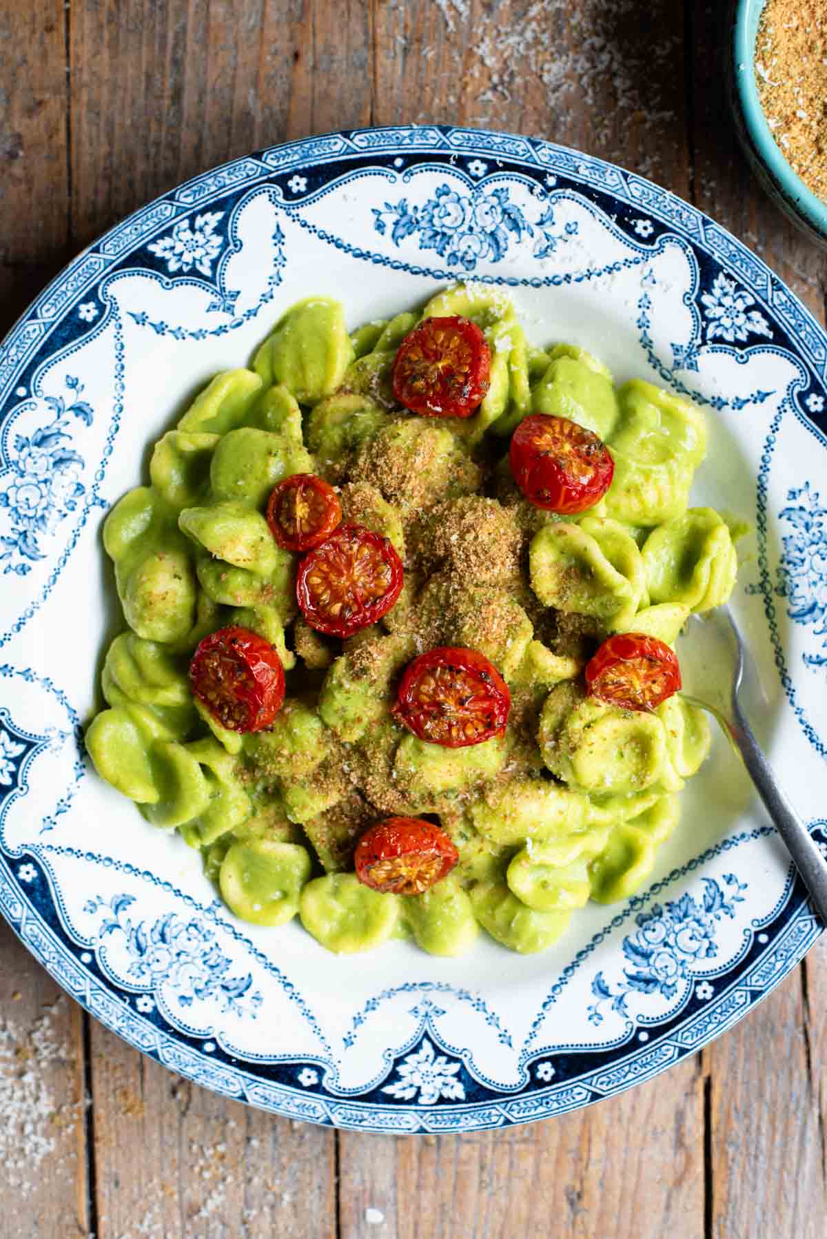 An overhead shot of orecchiette pasta in a vibrant green zucchini sauce with roasted cherry tomatoes on top.