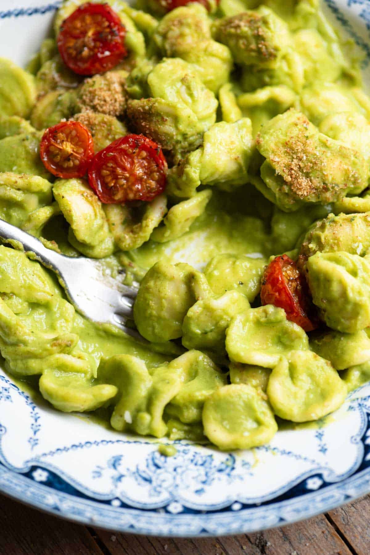 A close up of orecchiette in a smooth vibrant green zucchini sauce with roasted tomatoes on top.