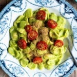 Orecchiette in a vibrant green zucchini sauce topped with roasted cherry tomatoes. The bowl is blue and white vintage style.