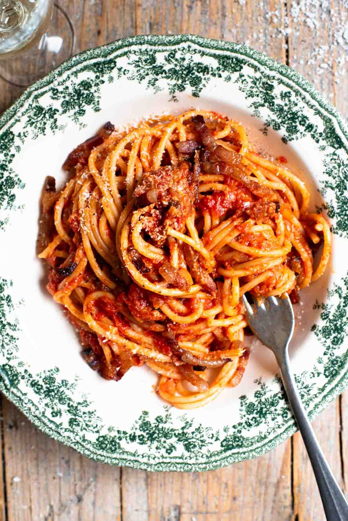 An overhead shot of spaghetti in a green and white vintage style bowl with a tomato and pancetta sauce. The background in rustic wood.
