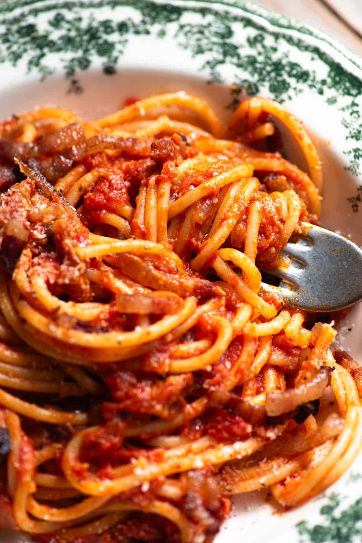 A close up of a fork in a bowl with tomato spaghetti topped with pecorino and pancetta.