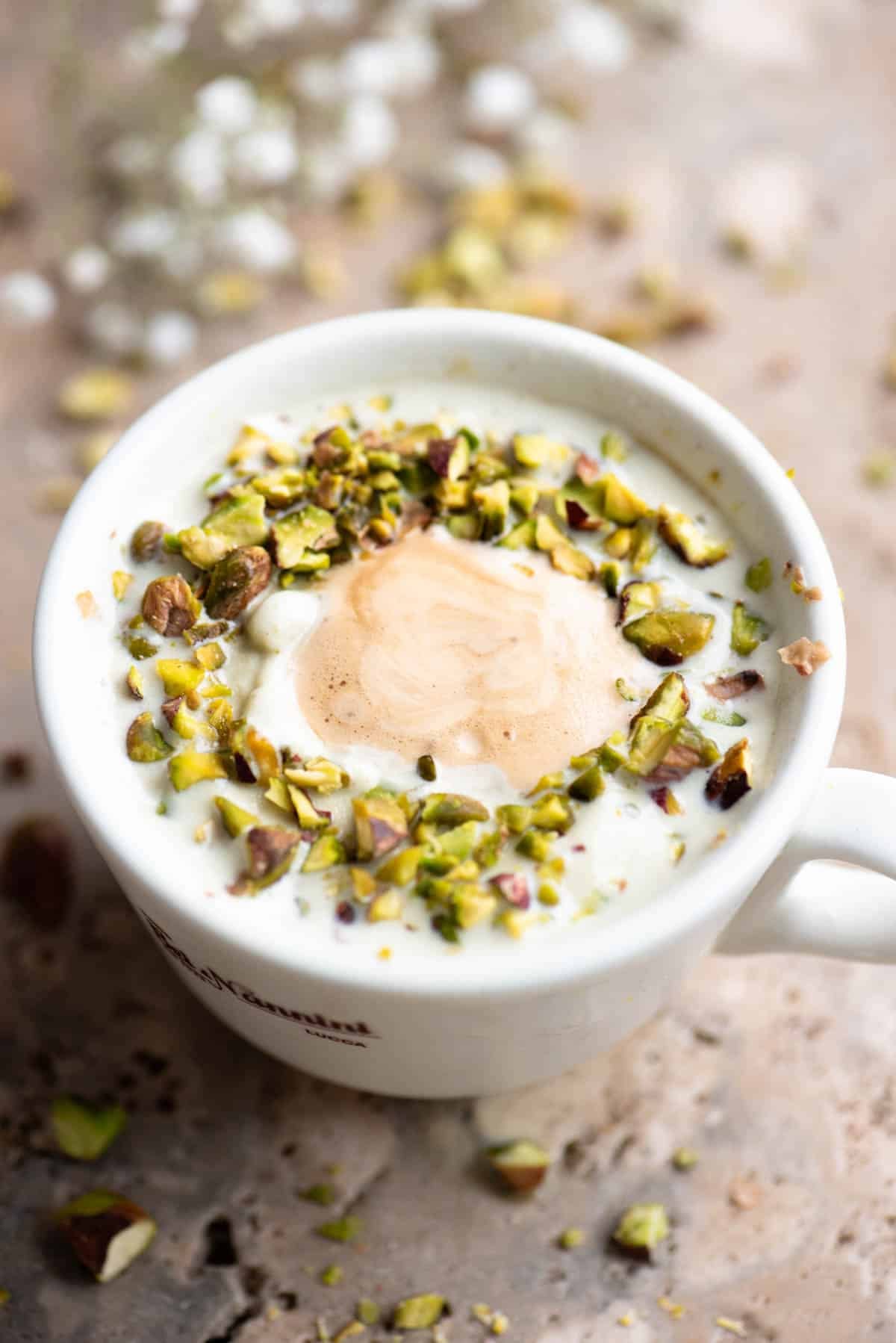 A pistachio affogato topped with chopped pistachios on a travertine surface.