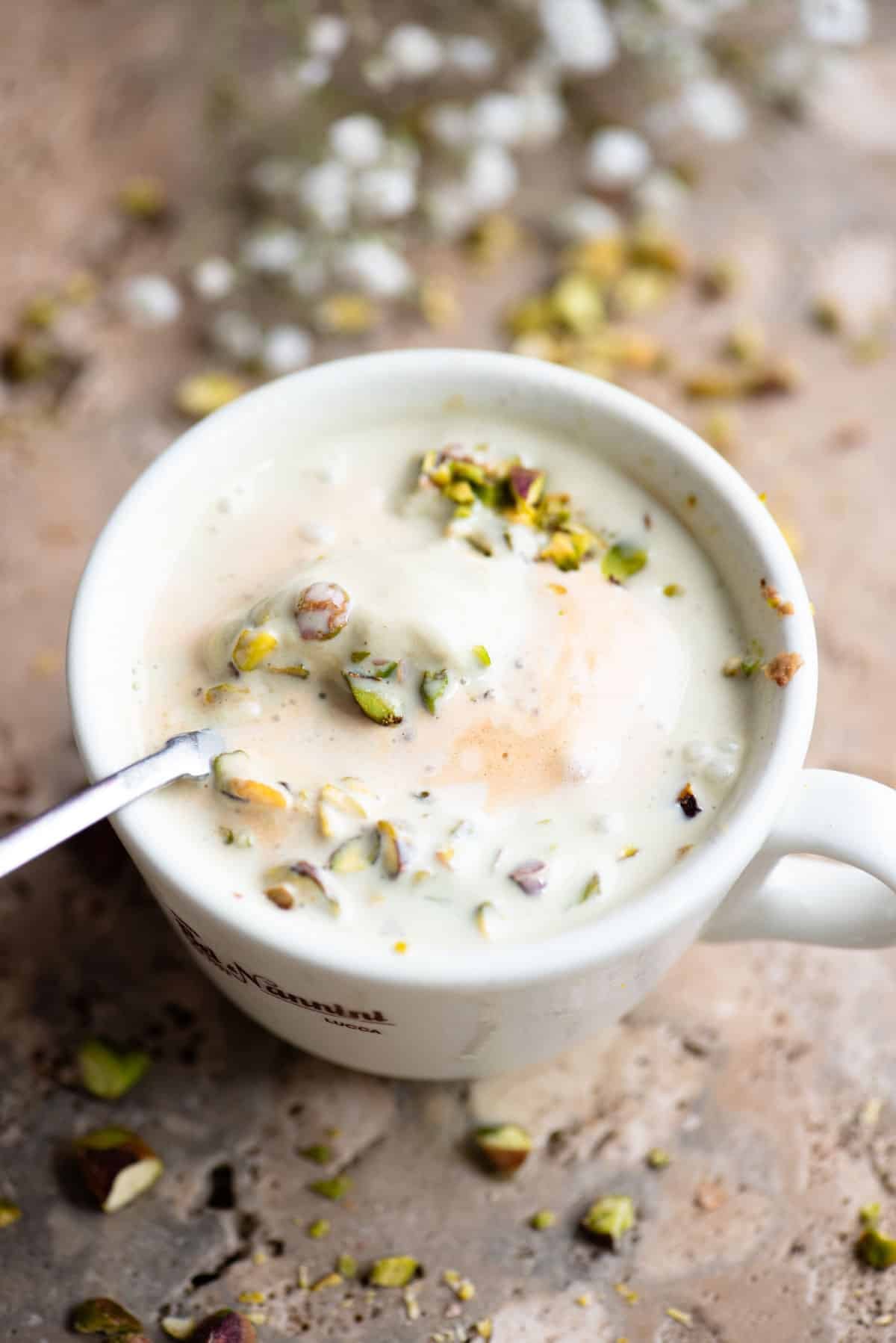 A pistachio affogato mixed in a mug with a spoon inside.