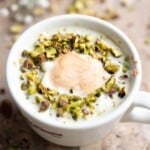 A pistachio affogato in a white mug topped with chopped pistachios.