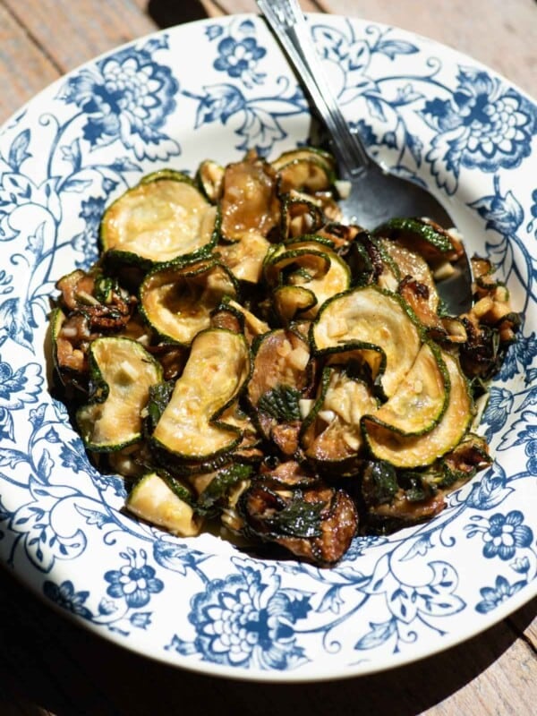 A blue and white floral bowl filled with fried marinated zucchini and a spoon.