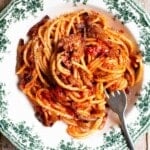 Tomato spaghetti with pancetta and pecorino in a green and white floral bowl with a fork.