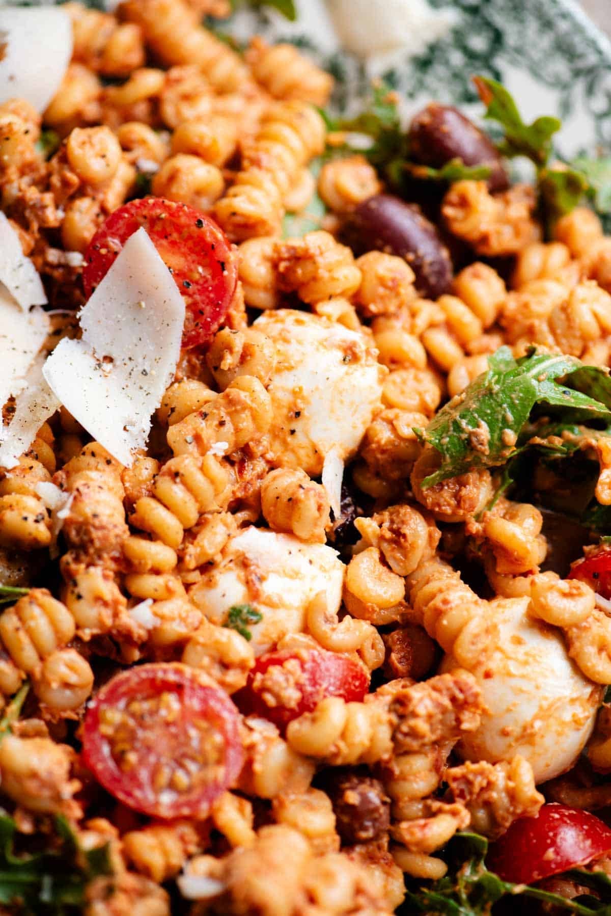 A close up of a pasta salad with a sun-dried tomato sauce, olives, mozzarella and fresh cherry tomatoes.