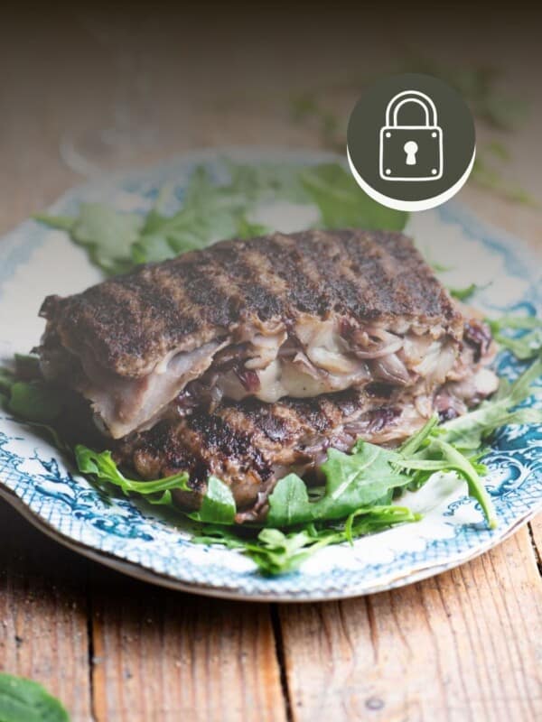 Two slices of stuffed beef stuffed with cheese, radicchio and porchetta on top of each other on a blue plate garnished with arugula. The top corner has a padlock sign to signify a member only recipe.