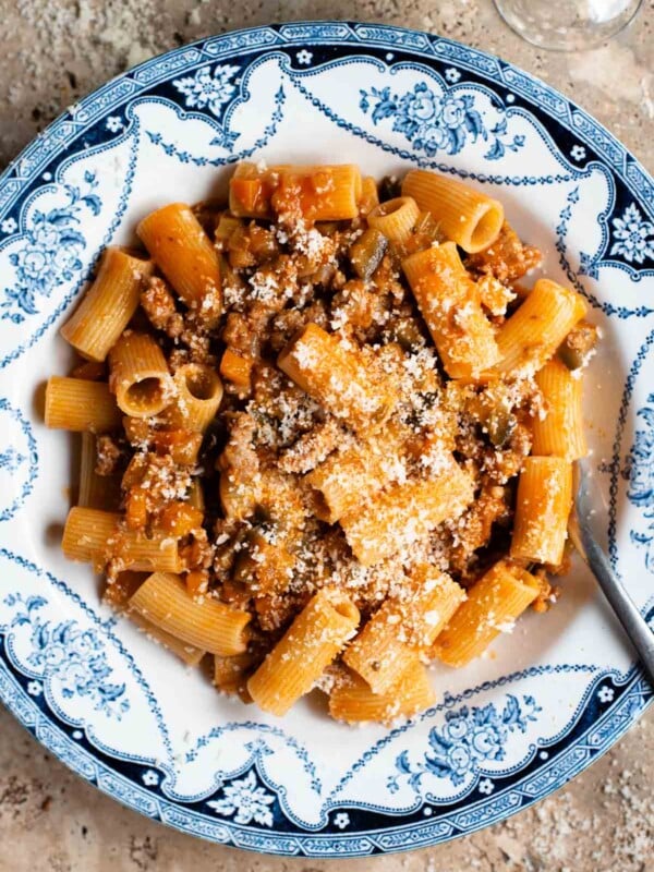 An overhead shot of rigatoni pasta with a sausage and eggplant ragu in a blue and white bowl on a travertine surface.