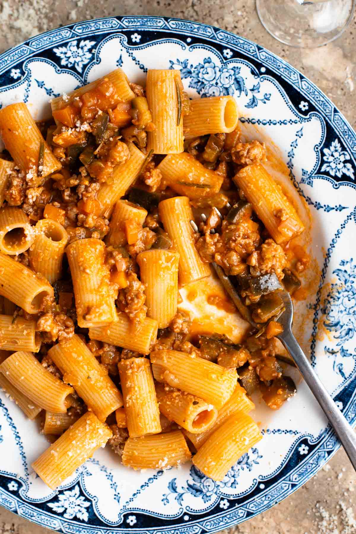 A close up of rigatoni pasta with a sausage and eggplant ragu in a blue and white bowl.