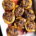 Baked peaches stuffed with amaretti cookies and dark chocolate in a white baking dish on a rustic wooden background.