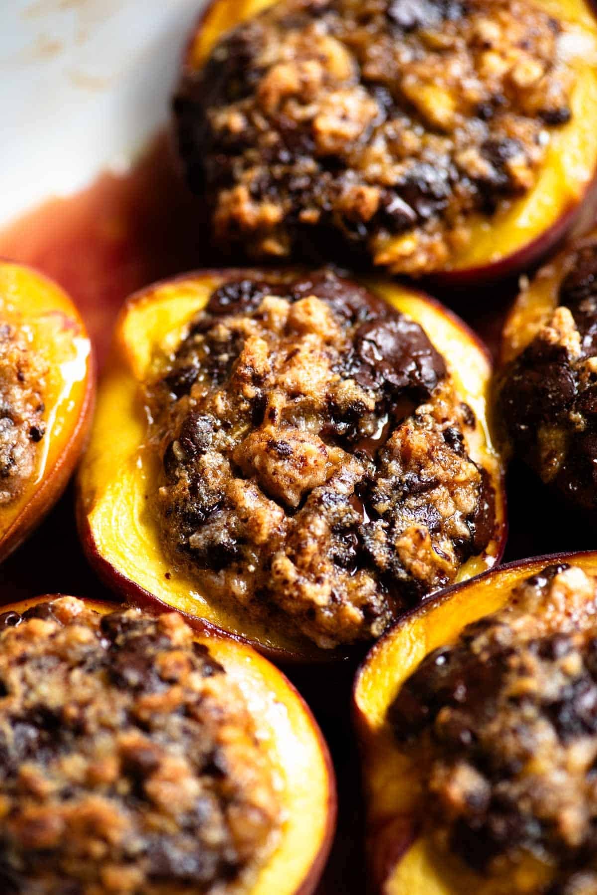 A close up of a baked peach stuffed with amaretti cookies and chocolate in a baking dish.
