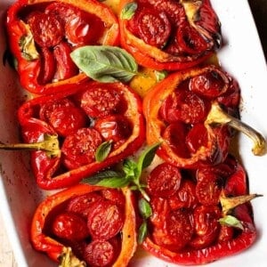 A close up cropped square image of roasted red bell peppers stuffed with cherry tomatoes, basil, garlic and anchovies.
