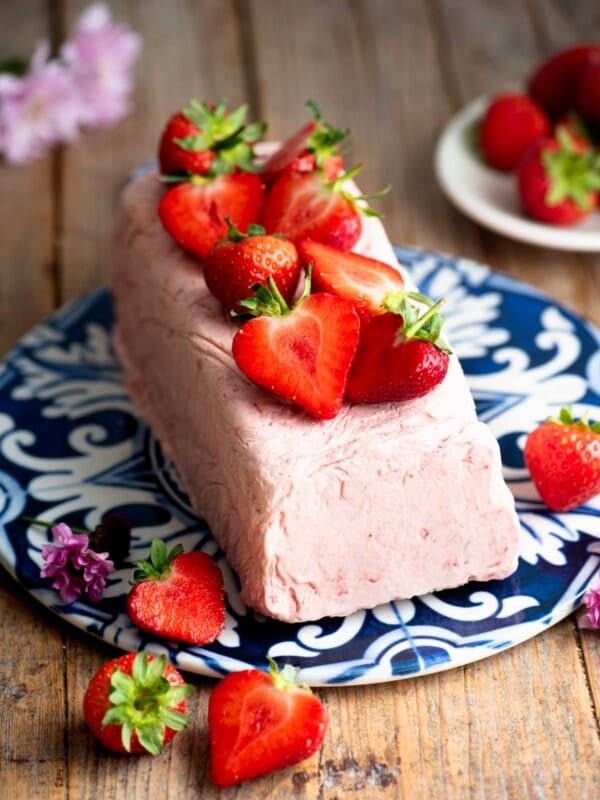 Strawberry semifreddo on a blue and white ceramic serving board topped with cut strawberries.