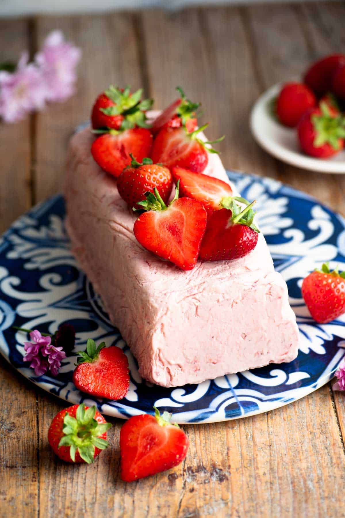 Strawberry semifreddo on a blue and white ceramic serving board topped with cut strawberries.