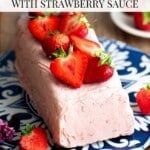 Strawberry semifreddo on a blue and white serving board topped with fresh strawberry. The table is rustic wood.