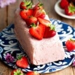 Strawberry semifreddo on a blue and white ceramic board topped with fresh cut strawberries sitting on a rustic wooden table.