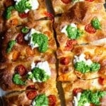 An overhead shot of a focaccia cut into 8 slices and topped with cherry tomatoes, pesto and burrata.
