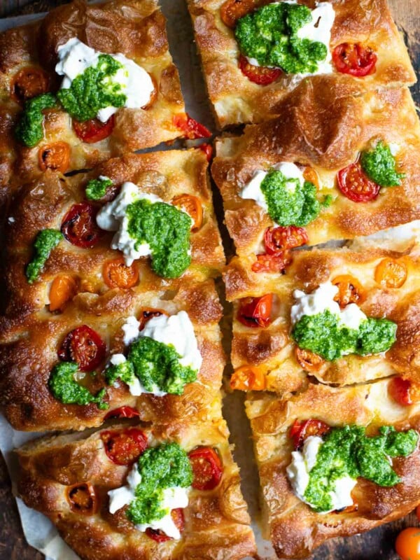 An overhead shot of a focaccia cut into 8 slices and topped with cherry tomatoes, pesto and burrata.