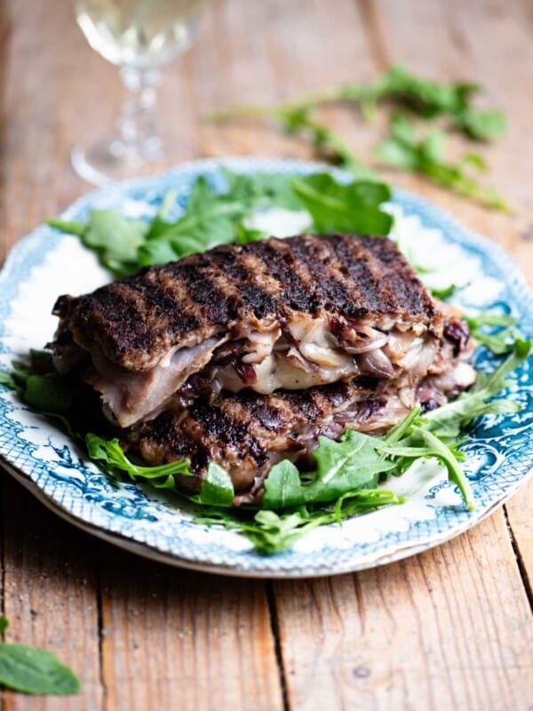 Two slices of stuffed beef stuffed with cheese, radicchio and porchetta on top of each other on a blue plate garnished with arugula.
