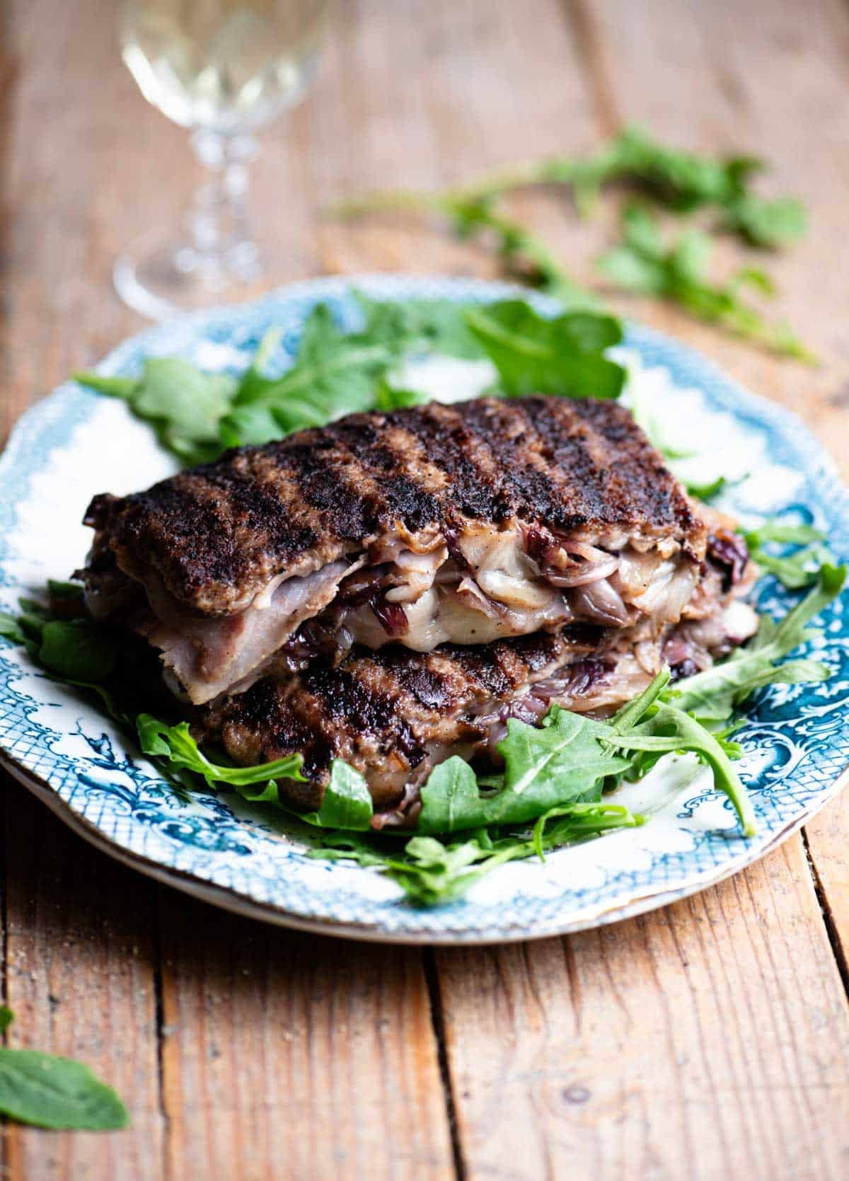 Two slices of stuffed beef stuffed with cheese, radicchio and porchetta on top of each other on a blue plate garnished with arugula.