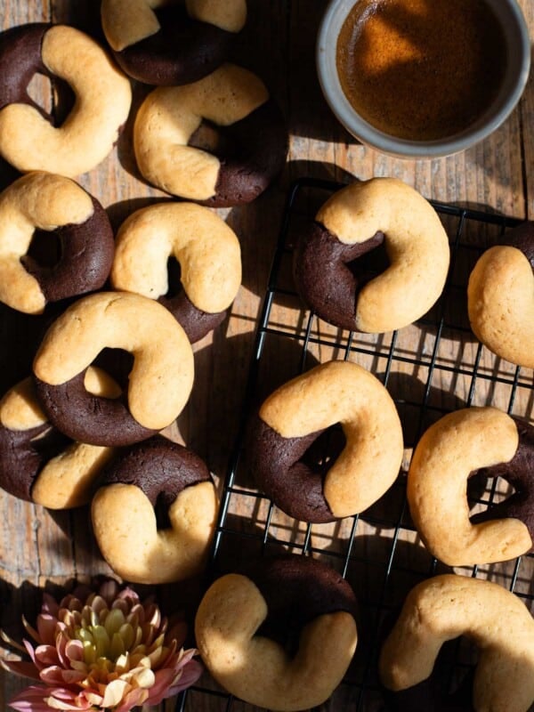An overhead shot of Italian abbracci cookies (chocolate and cream) on a rustic wooden surface with an espresso at the side.