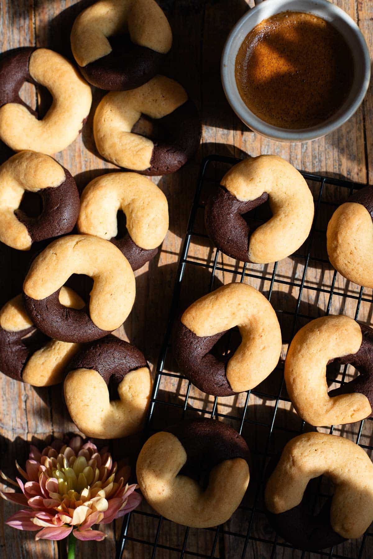 An overhead shot of Italian abbracci cookies (chocolate and cream) on a rustic wooden surface with an espresso at the side.