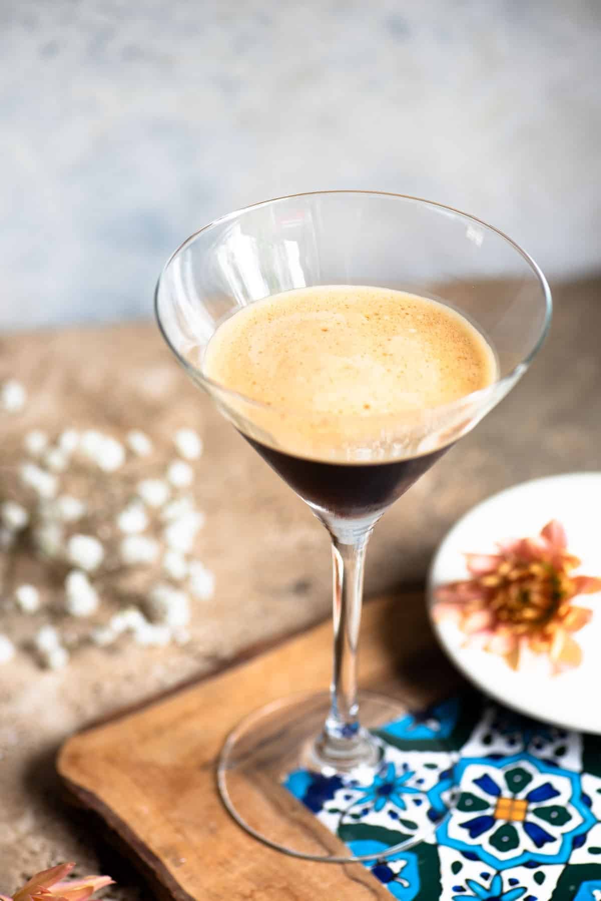 A martini glass filled with an iced coffee on a patterned tile with flowers at the side.