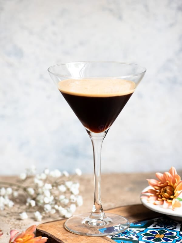 A martini glass filled with an Italian iced coffee sitting on a wooden table with flowers around.