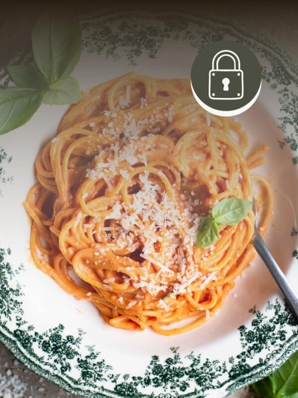 Cherry tomato and ricotta spaghetti in a floral bowl. The top of the image has a gradient fade and there is a padlock symbol in the top right to signify a member-only recipe.