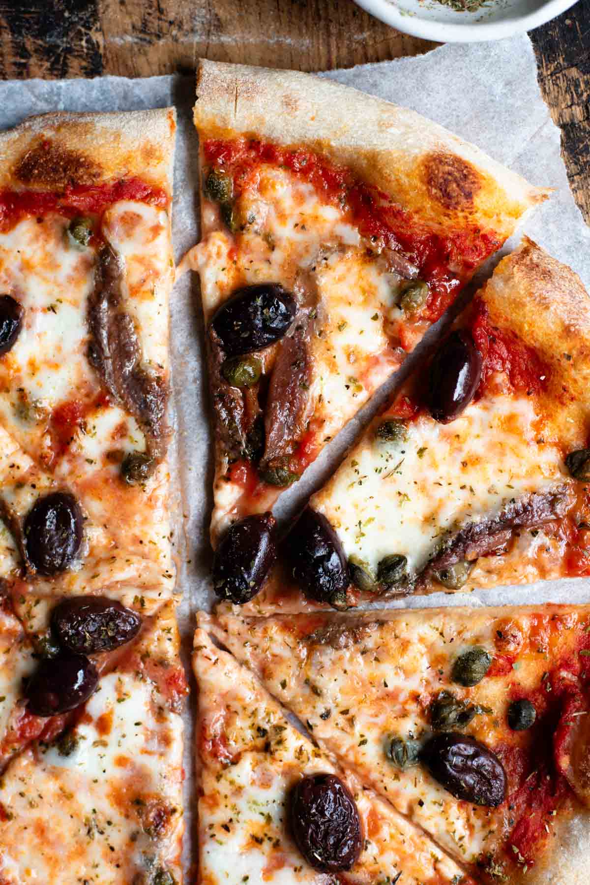 A close up of slices of pizza with mozzarella, tomato, olives, capers and anchovies.
