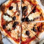 An overhead shot of a pizza topped with mozzarella, olives, capers, and anchovies on a rustic wooden surface.