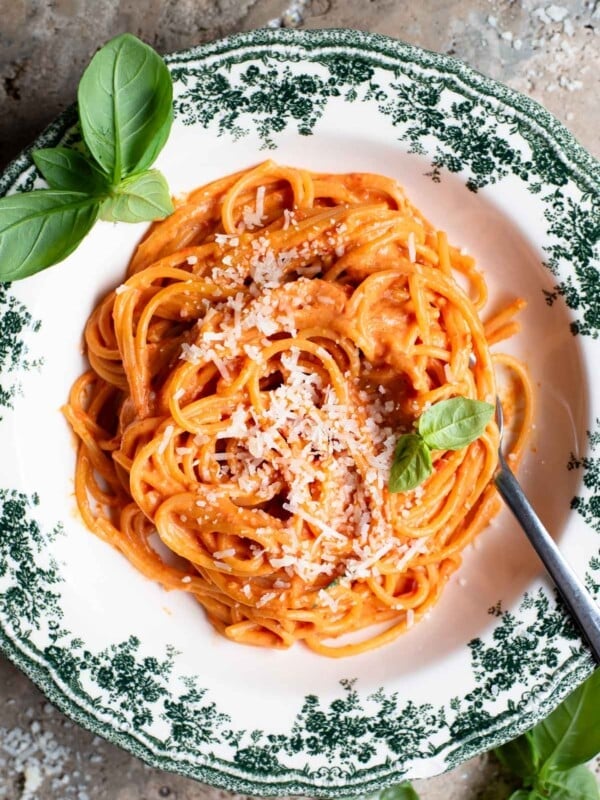 An overhead shot of roasted cherry tomato and ricotta spaghetti in a green floral bowl with basil scattered around.