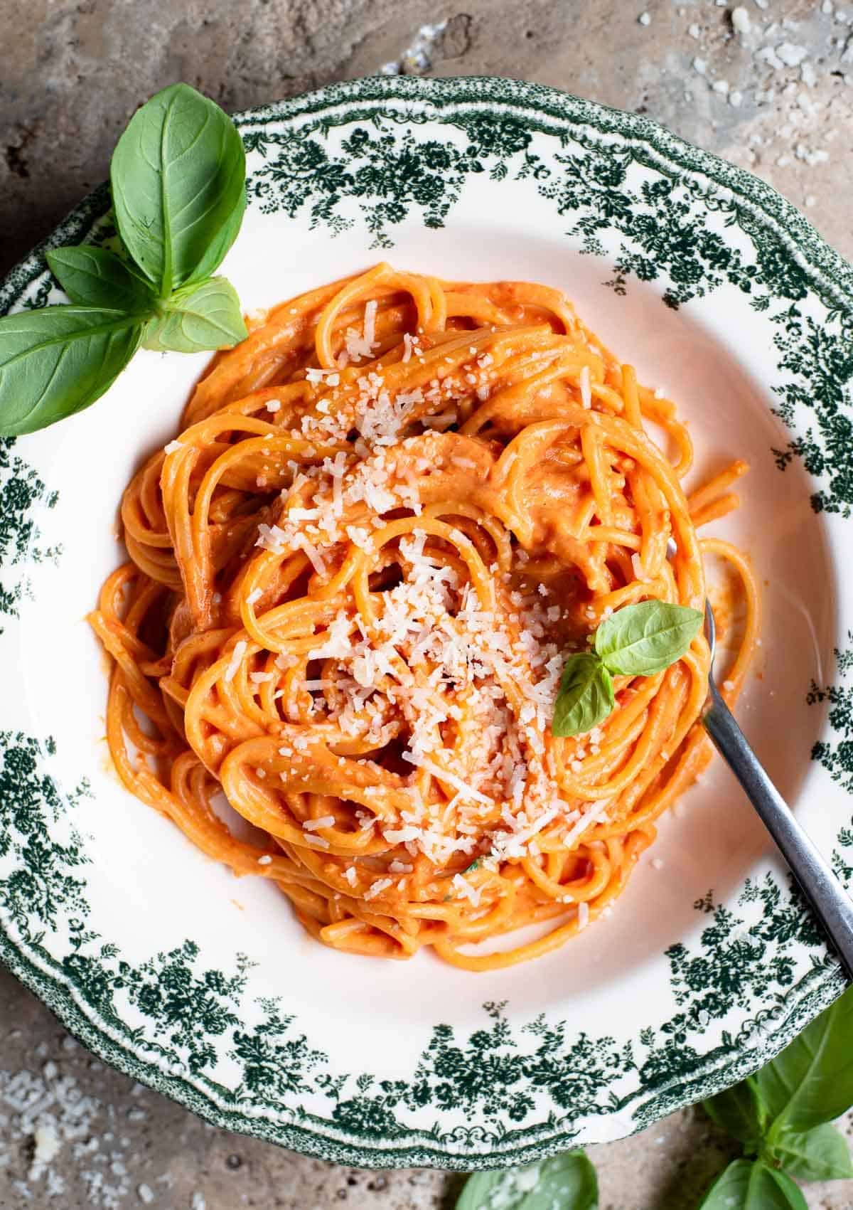 An overhead shot of roasted cherry tomato and ricotta spaghetti in a green floral bowl with basil scattered around.