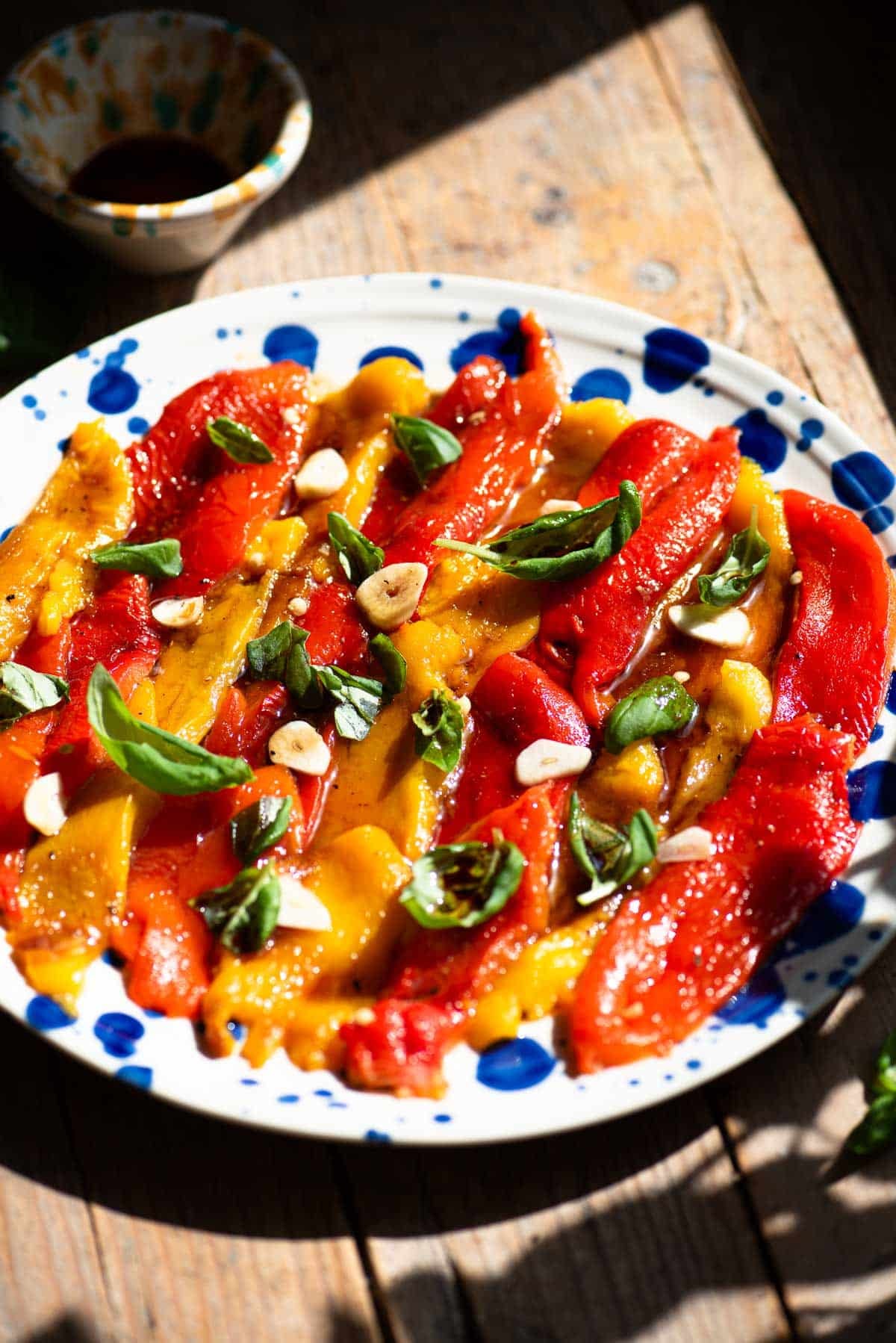Italian marinated roasted peppers on a blue and white plate topped with garlic and basil. The background is rustic wood.