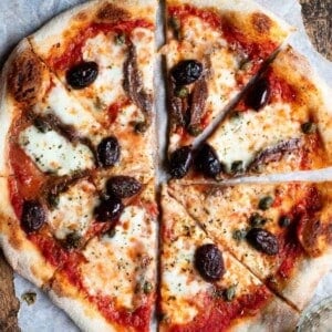 A close up of a pizza cut into slices topped with olives, capers ad anchovies.