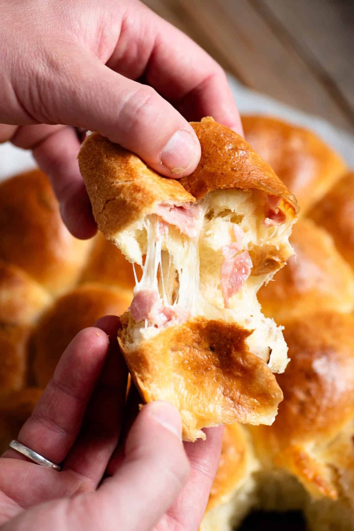 A hand tearing open a piece of danubio salato to show the cheese pull and ham inside.