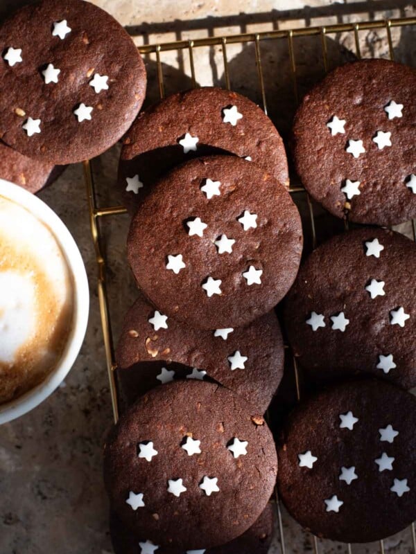 An overhead shot of lots of Pan di Stelle Italian cookies on a cooling rack with a cappuccino at the side.